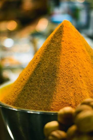 Dried turmeric roots and leaf powder in shallow bowls beside a closed paper folder and a pen on a pale desk